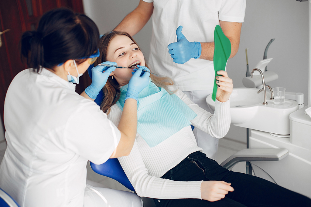 Dentist performing braces check while patient looks in mirror