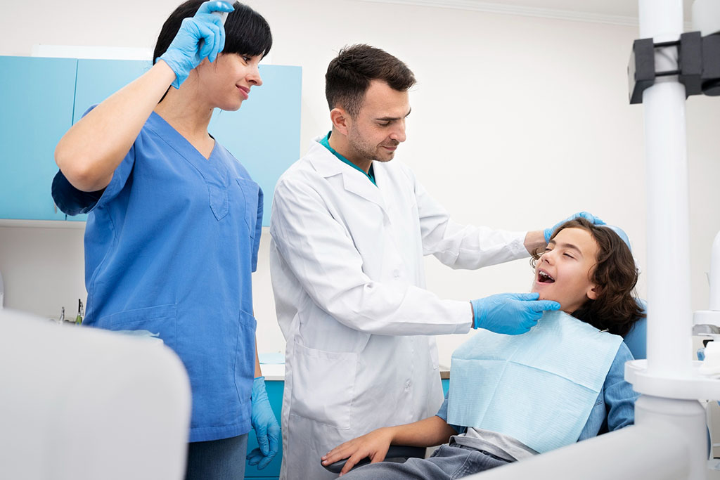 Dentist examining young patient with dental assistant nearby