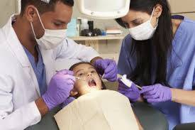 Child with mouth open having her teeth checked by dentist and assistant
